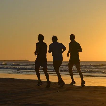 Three men running on a beach at sunset